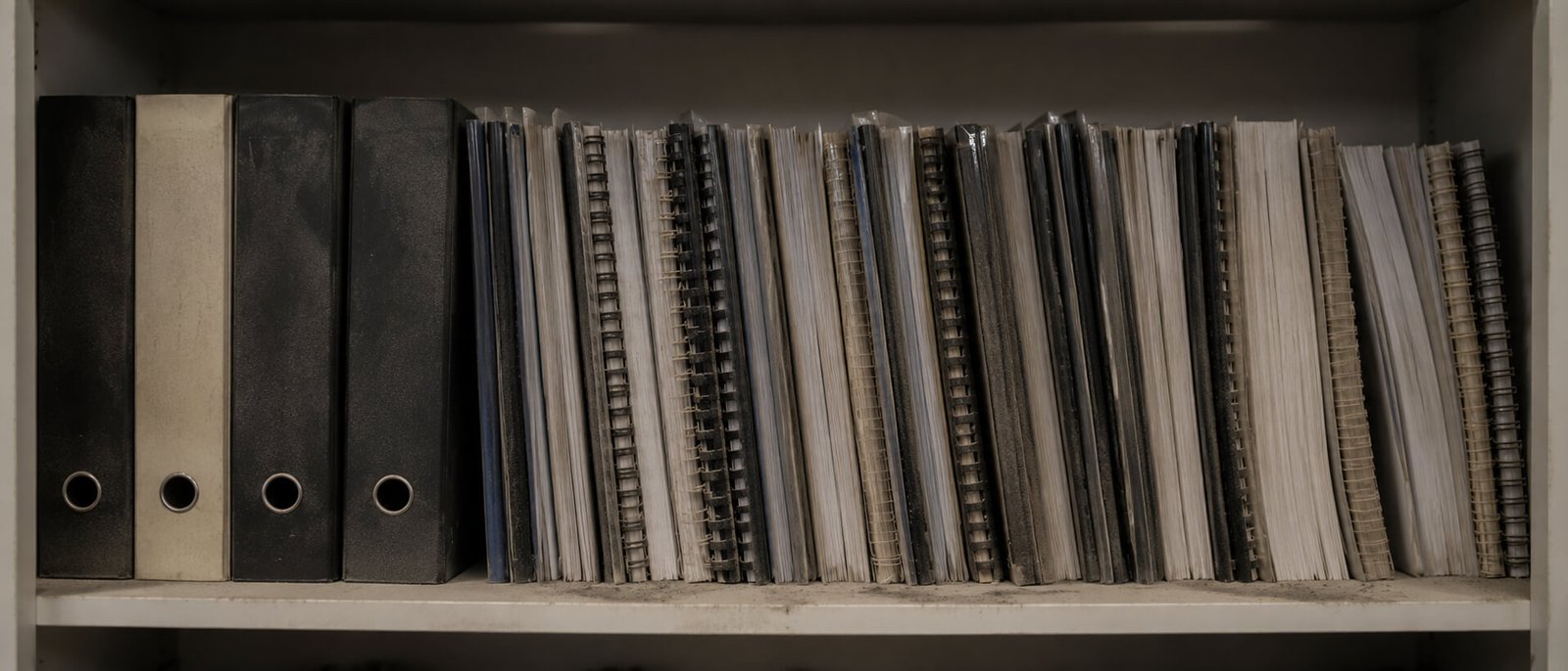 A shelf of thick spiral-bound presentation decks and binders, dusty and untouched